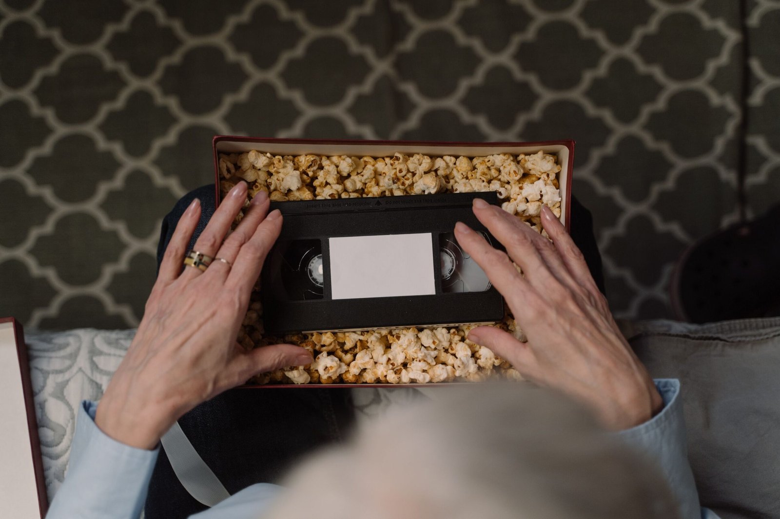 Top view of hands holding a VHS tape surrounded by popcorn in a vintage setting.