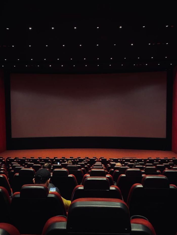 The Biggest Movies Coming in September 2026: What to Watch This Month Dimly lit cinema hall with red seats and a blank screen. Minimal audience.